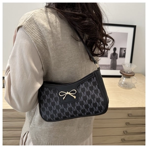 Dettaglio di una borsa sottobraccio nera con chiusura a fiocco dorata su una modella