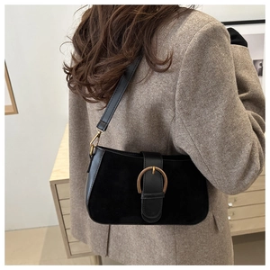 Close-up of matte black shoulder bag featuring vintage gold buckle on brown blazer