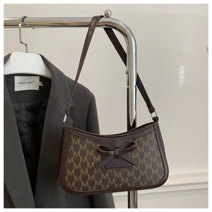 Detail of retro underarm bag with M-letter print and central bow on a metal hanger