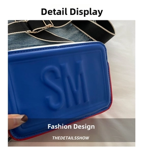 Close-up of blue embossed SM logo on denim crossbody bag with striped shoulder strap
