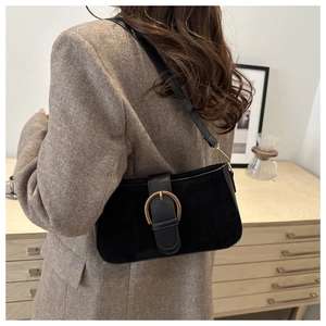 Detail of suede and leather crossbody bag with gold buckle on a model in blazer