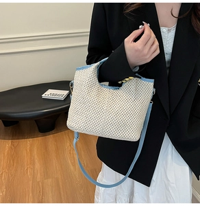Chic beige woven straw tote bag with sky blue leather straps shown on a model