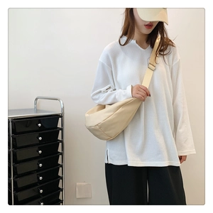 Sac bandoulière en toile beige en forme de croissant porté par un mannequin de mode