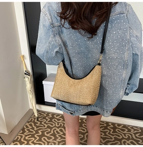 Detailed view of woven straw hobo bag with black leather trim worn on the shoulder