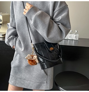 Détail d'un sac seau matelassé noir avec fermoir doré et pendentif nœud en peluche marron