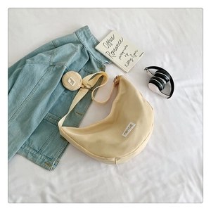 Détail d'un sac hobo beige avec pochette, stylisé avec des livres et des écouteurs