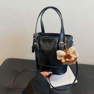 Sac seau noir à la mode avec breloque en peluche sur un banc en cuir, style minimaliste