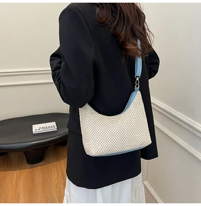 Detail of hand-woven straw tote with light blue trim and gold buckle on a model shoulder