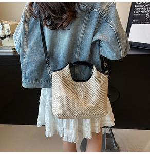 Close-up of beige woven tote bag with black leather handles and long shoulder strap