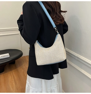 Detail of woven straw hobo bag with light blue leather straps and crescent shape structure