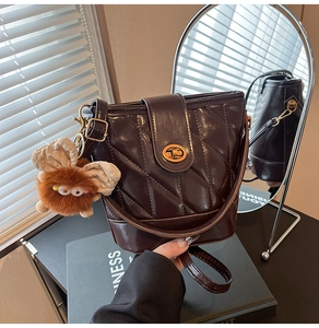Détail du sac seau marron café avec surpiqûres, fermoir doré et breloque peluche