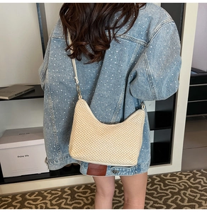 Close-up of beige woven crescent bag with zip closure on model in denim jacket