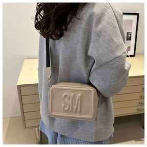 Detailed view of cream crossbody bag with embossed SM letters and wide canvas strap