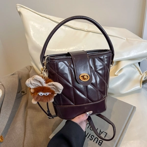 Sac seau matelassé violet foncé avec détails dorés et breloque peluche sur fond chic