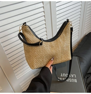 Detail of woven straw crescent bag featuring black leather trim and golden metal zippers