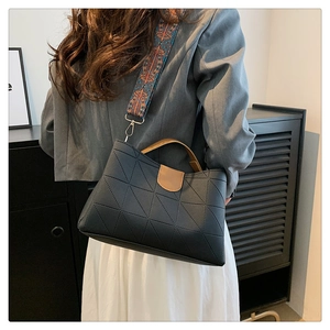 Detail of black geometric PU leather handbag featuring contrast handles and woven strap