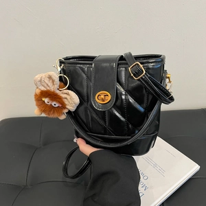 Sac seau matelassé noir moderne avec fermoir doré et breloque peluche sur gris