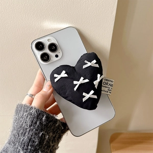 Detail showing plush black heart phone grip with a white bow on a white smartphone