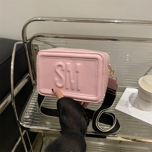 Pink rectangular crossbody bag with embossed SM letters and wide contrast shoulder strap