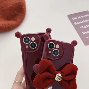 Deep burgundy iPhone case with velvet bow and gold rose button detail closeup