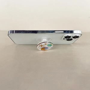 Detail of glitter starry planet phone socket stand showing extendable grip on a white phone