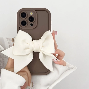 Coque iPhone marron avec un grand nœud en tissu crème tenue par un mannequin élégant