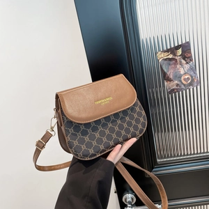 Sacoche selle vintage en cuir marron avec imprimé chaîne tenue par un mannequin élégant