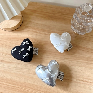 Detailed view of heart-shaped fabric phone grips in black, white and silver on wooden desk