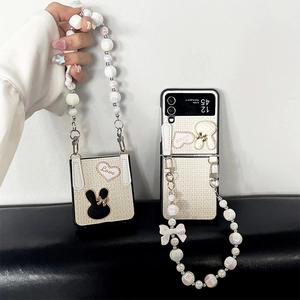 Detail showing white quilted fabric Samsung Galaxy Z Flip case with heart embroidery and pearl chain