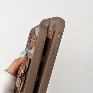 Dettaglio della cover iPhone marrone con glitter e orsetto di peluche 3D con fiore