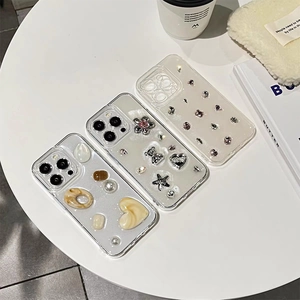 Three transparent iPhone cases with glitter gems, silver bears, and rhinestones on a white table