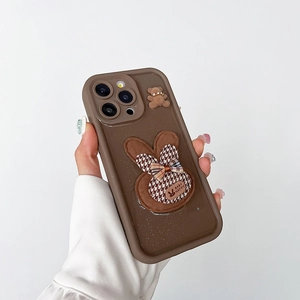 Dettaglio custodia iPhone marrone con coniglio glitter 3D e orsetto di peluche