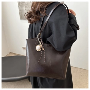 Detail of deep brown tote bag featuring glossy leather texture and baseball pendant decoration