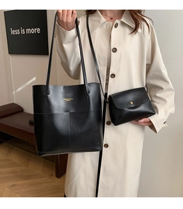 Detail of large black leather tote bag set with golden lettering and crossbody bag