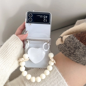 Detail of Galaxy Z Flip 6 clear case with white heart charm and cream pearl wrist strap