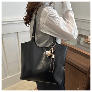 Detail of minimalist black faux leather tote bag with baseball themed keychains and charms