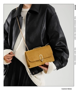 Detail of mustard yellow suede crossbody bag with gold U-shaped buckle and chain strap