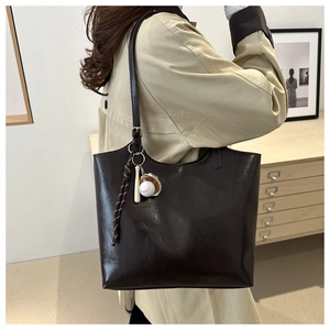 Detail of a large brown leather tote bag with sports charms and woven strap decoration