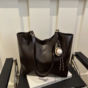 Minimalist deep brown faux leather tote bag with a sporty charm on a wooden chair