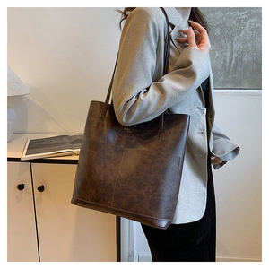 Detailed view of deep brown vintage faux leather tote bag worn with a grey blazer
