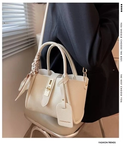 Detail of beige lychee leather bucket bag with gold hardware and decorative silk scarf