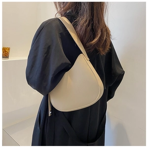 Minimalist beige underarm bag styled on black coat, showcasing smooth leather and crescent shape