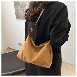 Close-up of brown suede shoulder bag with adjustable strap on a black coat outfit