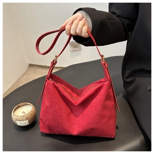 Detail of red suede hobo bag with golden adjustable buckle and zip closure shown in hand
