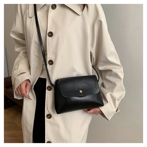 Detail of a minimalist black faux leather crossbody bag with a gold stud closure and strap