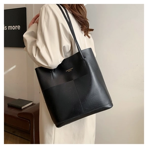 Detail of black pebbled leather tote bag featuring gold lettering and front pocket stitching