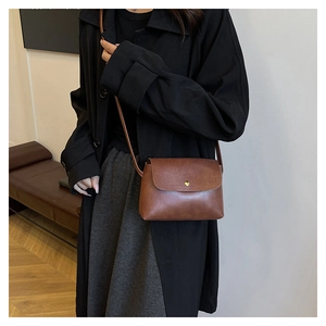 Detail of vintage brown leather tote bag with heart-shaped gold buckle worn on shoulder