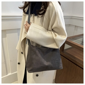 Detail view of a dark grey suede tote bag with matte finish on a wool coat model