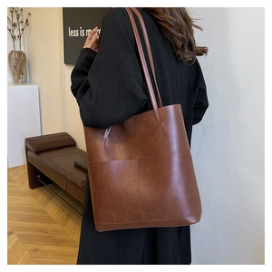 Detail of a deep brown leather tote bag showing fine stitching and minimalist slim handles