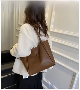 Brown leather tote bag worn by a model against a white interior background